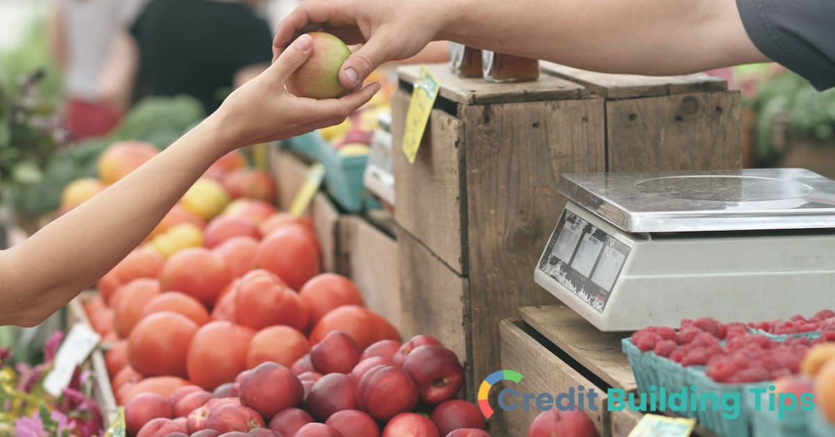 merchant handing fruit to customer using cash back credit card at grocery store