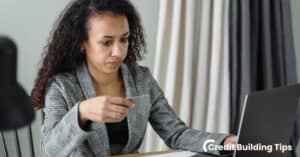 woman holding credit card looking at computer after noticing charge off